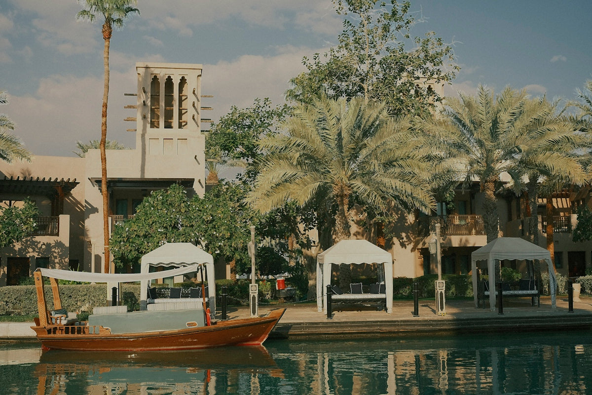 A wooden boat sits by buildings and palm trees