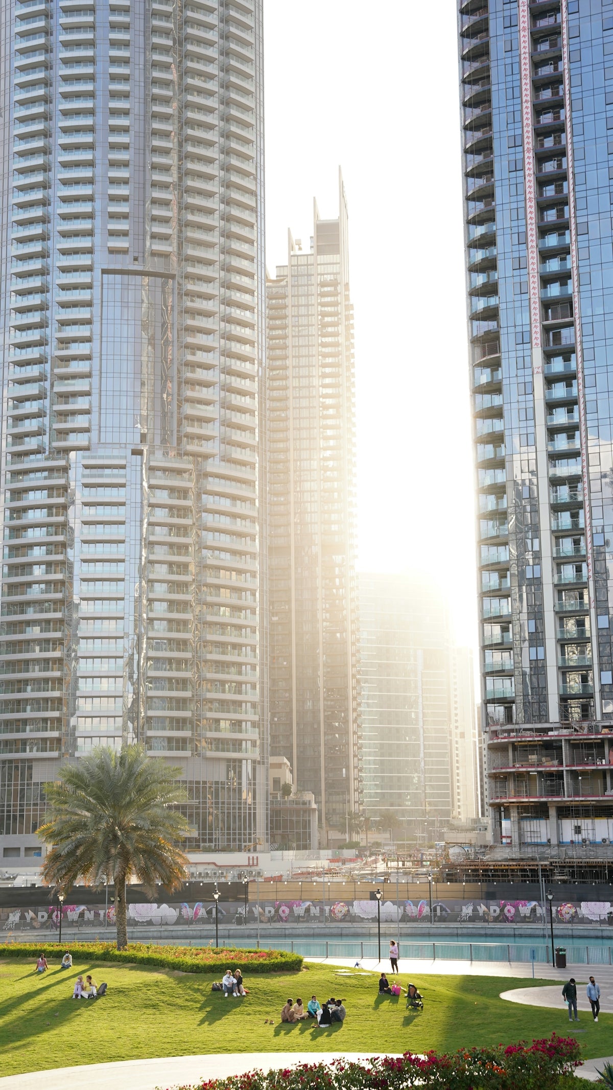 People relaxing on a green lawn in front of tall glass skyscrapers in Dubai